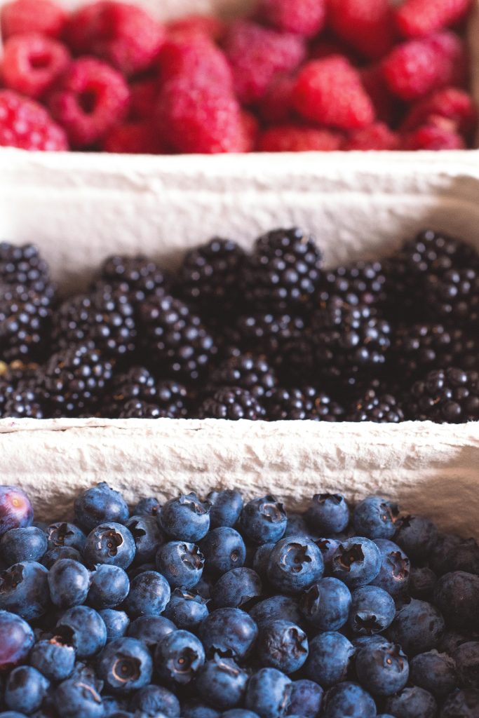 Close-up of fresh blueberries, blackberries, and raspberries at a market, showcasing vibrant colors and freshness.