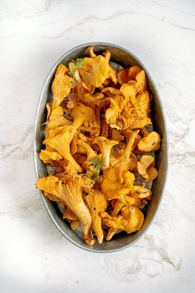 Top view of fresh chanterelle mushrooms in a stainless steel oval container on marble.
